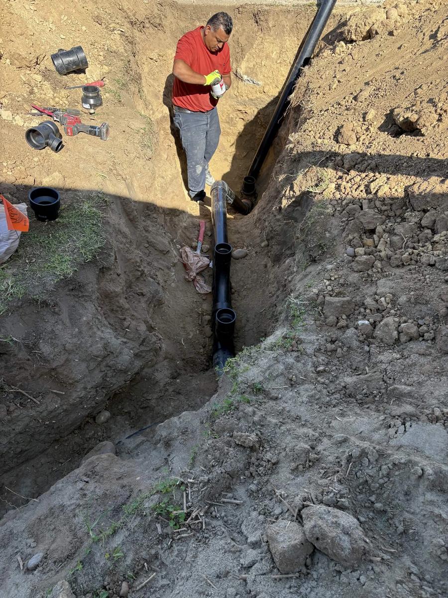 Viper technician priming and gluing ABS fittings at the bottom of a sewer trench