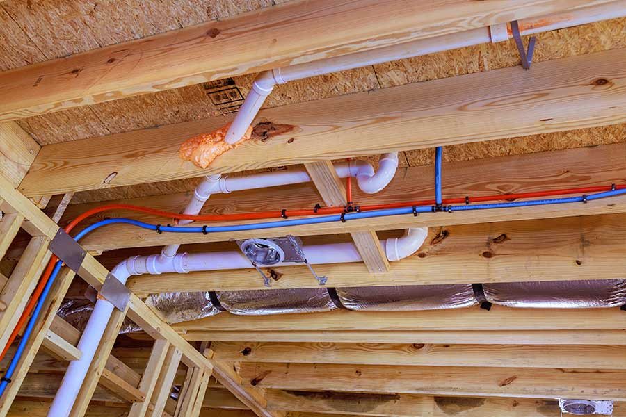 New construction plumbing rough-in with red and blue PEX water lines and PVC drains in wood framing