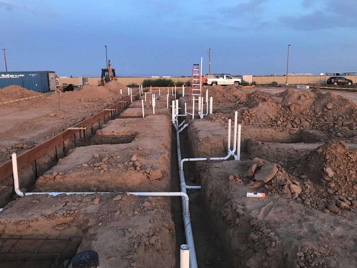 Ground-up construction site with underground plumbing rough-in and PVC stub-ups in trenches