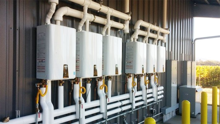 Commercial rack of six tankless water heaters with PVC venting and gas lines