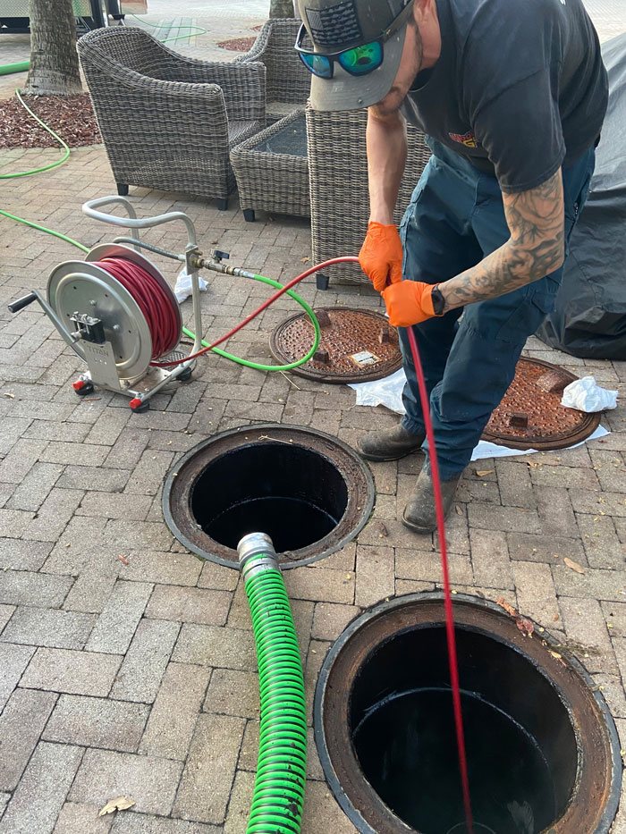 Technician hydro jetting through a manhole access point during a trenchless lining project
